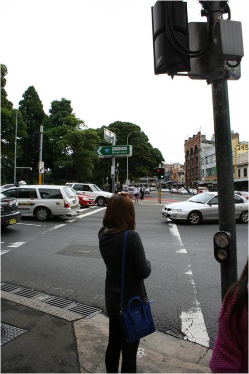 In a popular neighborhood a woman waits at abusy crossing for light to change.